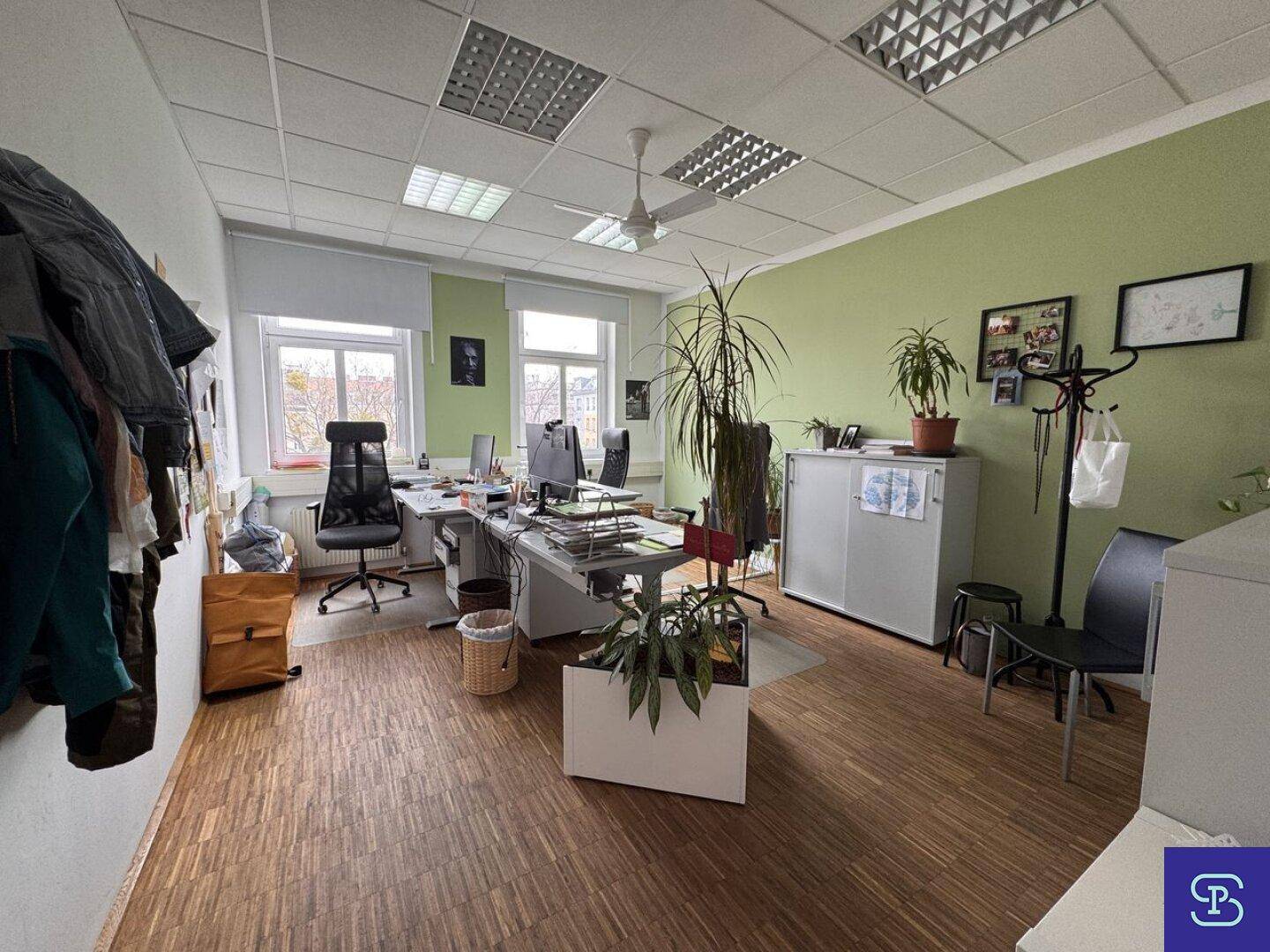 Großes Büro mit Holzparkett, Deckenventilator und mehreren Arbeitsplätzen, mit grüner Akzentwand.