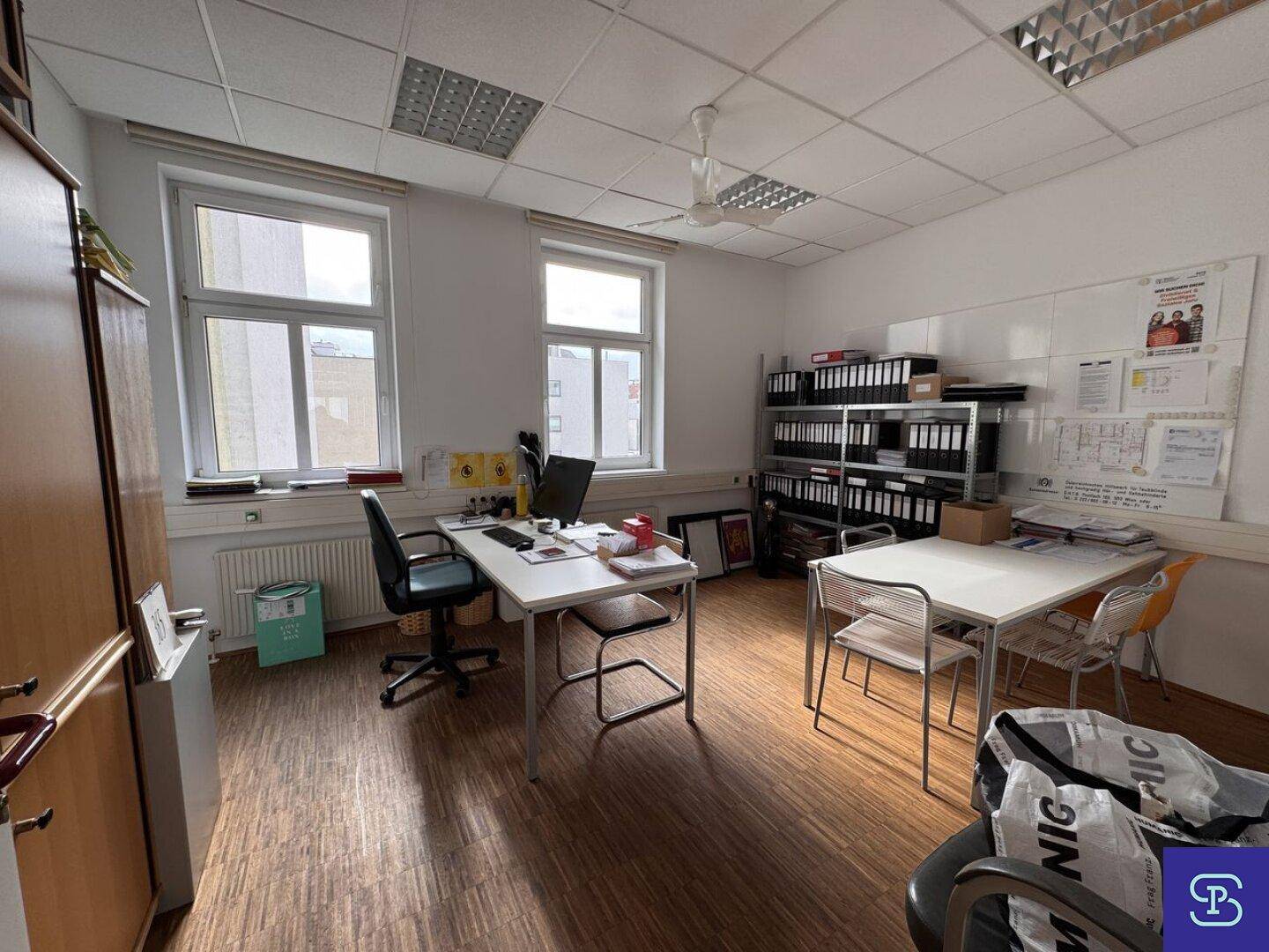 Geräumiges Büro mit Holzparkett, Deckenventilator und mehreren Arbeitsplätzen, mit großen Fenstern.