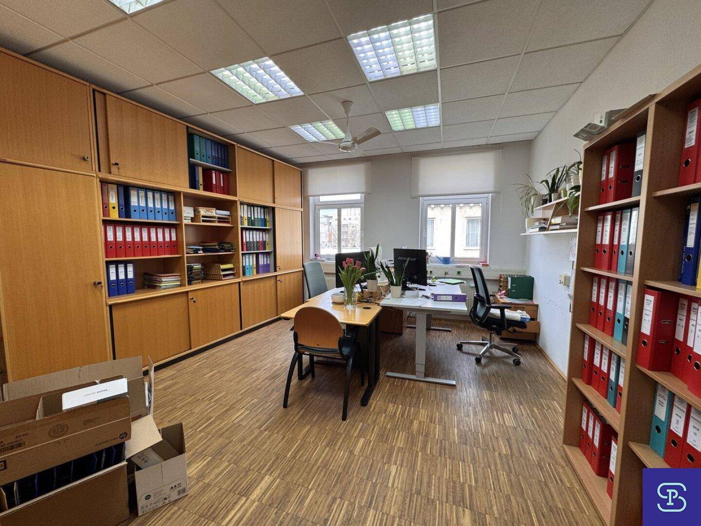 Großes Büro mit Holzparkett, Deckenventilator und mehreren Arbeitsplätzen, umgeben von Aktenschränken.