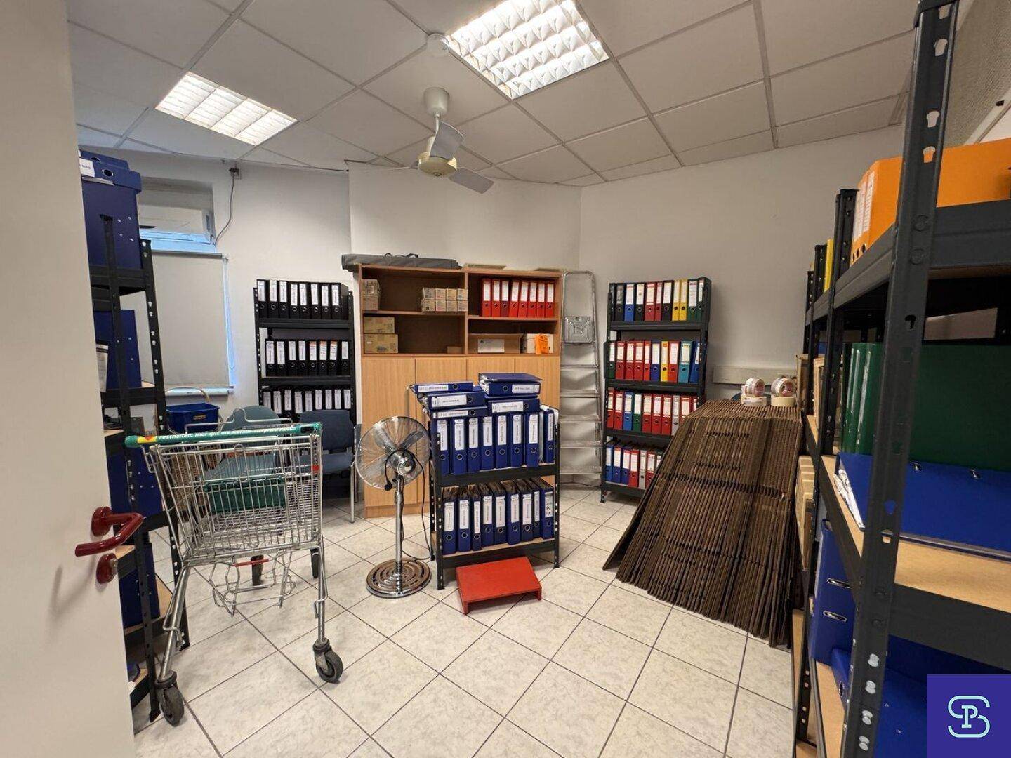 Lagerraum mit Fliesenboden, Metallregalen und vielen Aktenordnern, ideal für Archivierung.