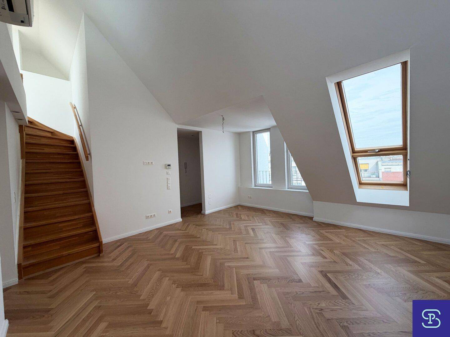 Geräumiges Dachgeschosszimmer mit Holztreppe, Fischgrätparkett und viel Tageslicht durch Dachfenster.