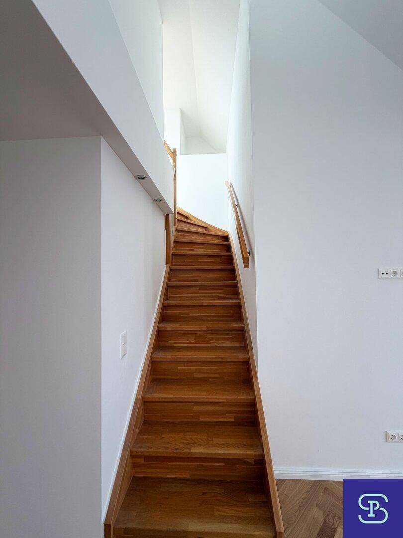 Elegante Holztreppe mit Handlauf, die die verschiedenen Ebenen des Dachgeschosses miteinander verbindet.
