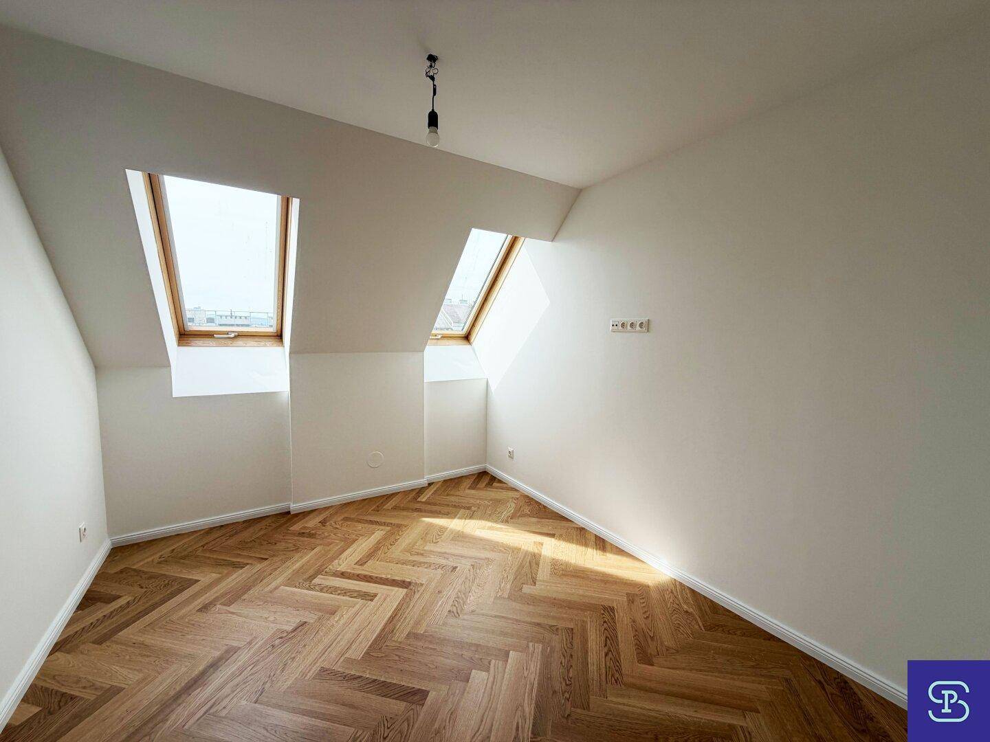 Lichtdurchflutetes Dachgeschosszimmer mit Fischgrätparkett und zwei Dachfenstern, ideal als Schlafzimmer.