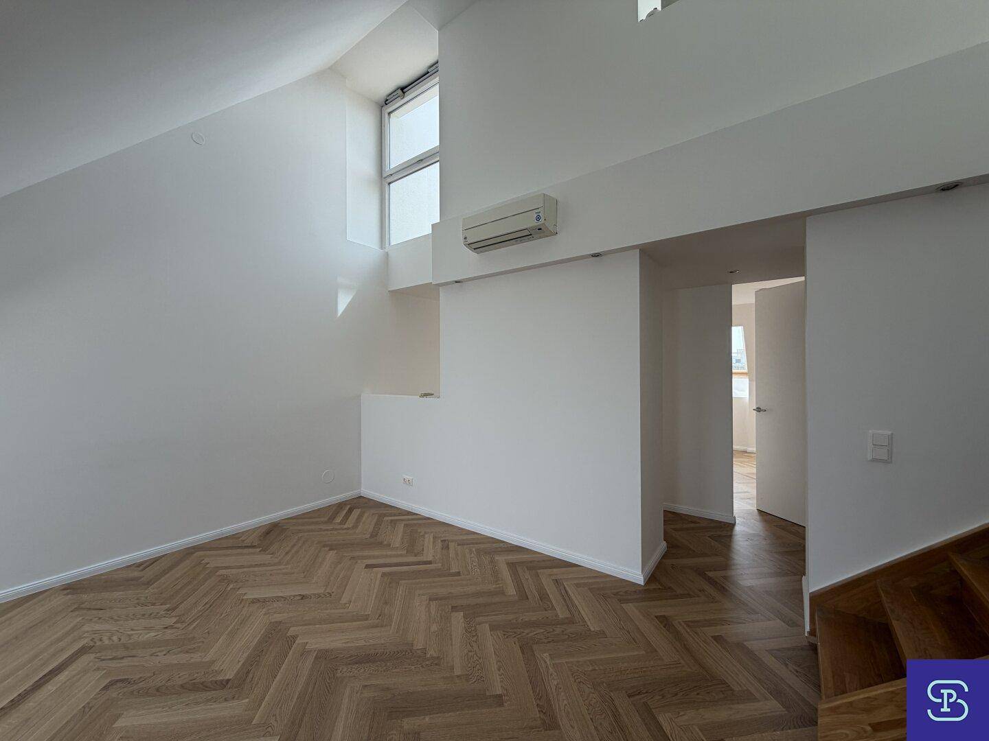 Modernes Dachgeschosszimmer mit Klimaanlage, Fischgrätparkett und hoher Decke, bereit für die Einrichtung.