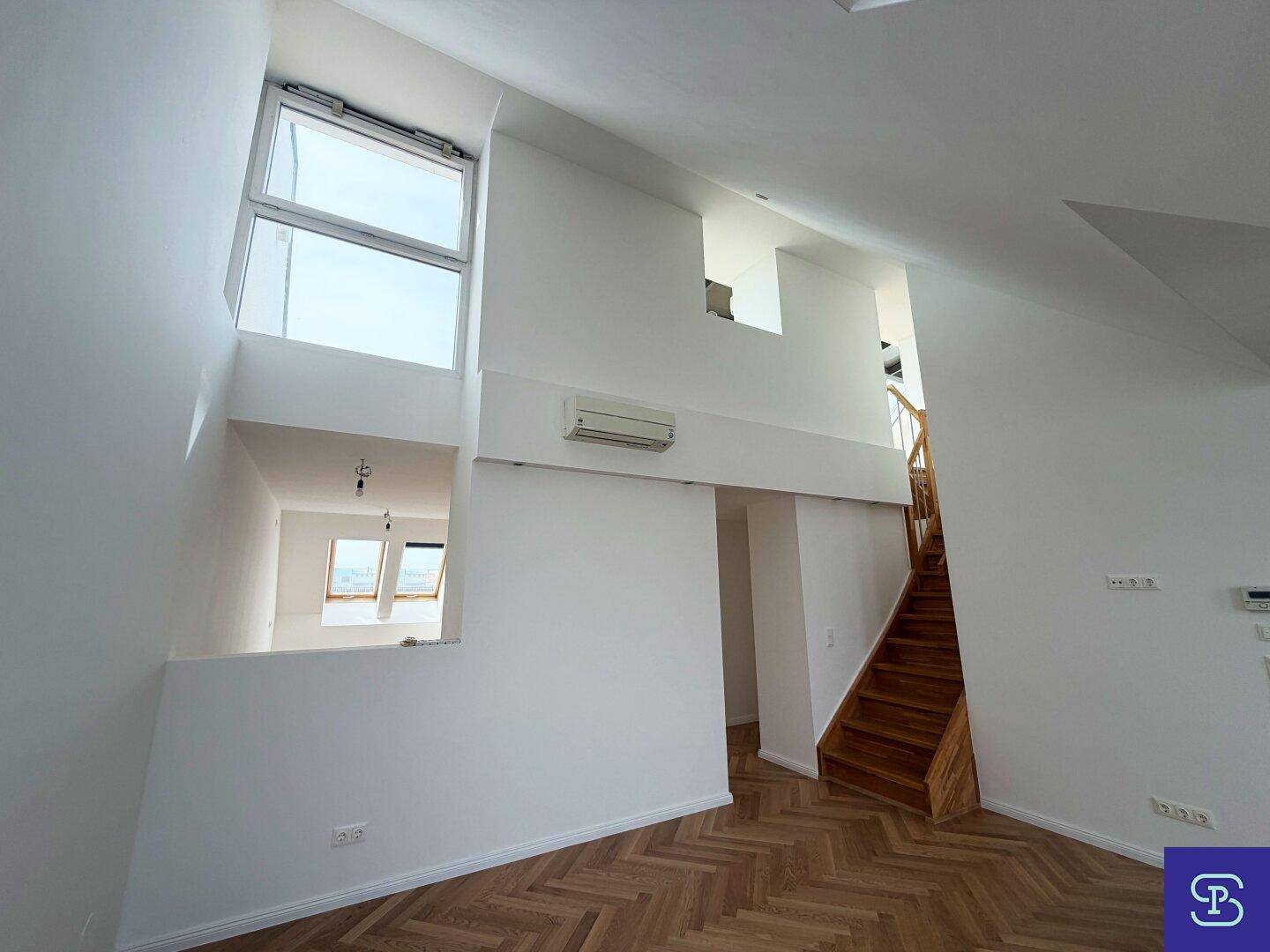 Offener Wohnbereich im Dachgeschoss mit Holztreppe, hohen Decken und mehreren Fenstern für viel Licht.