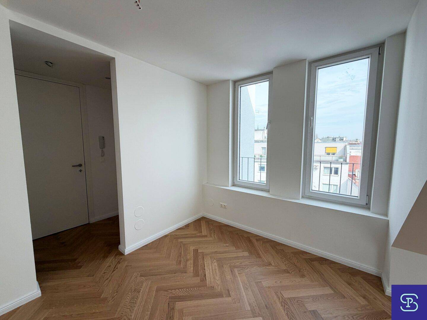 Heller Wohnbereich im Dachgeschoss mit Fischgrätparkett und Blick auf die Umgebung durch hohe Fenster.