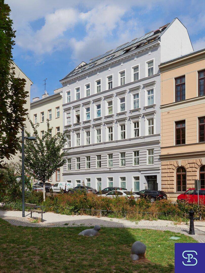 Historisches Wohngebäude mit klassischer Fassade und Bäumen im Vordergrund an einem sonnigen Tag.