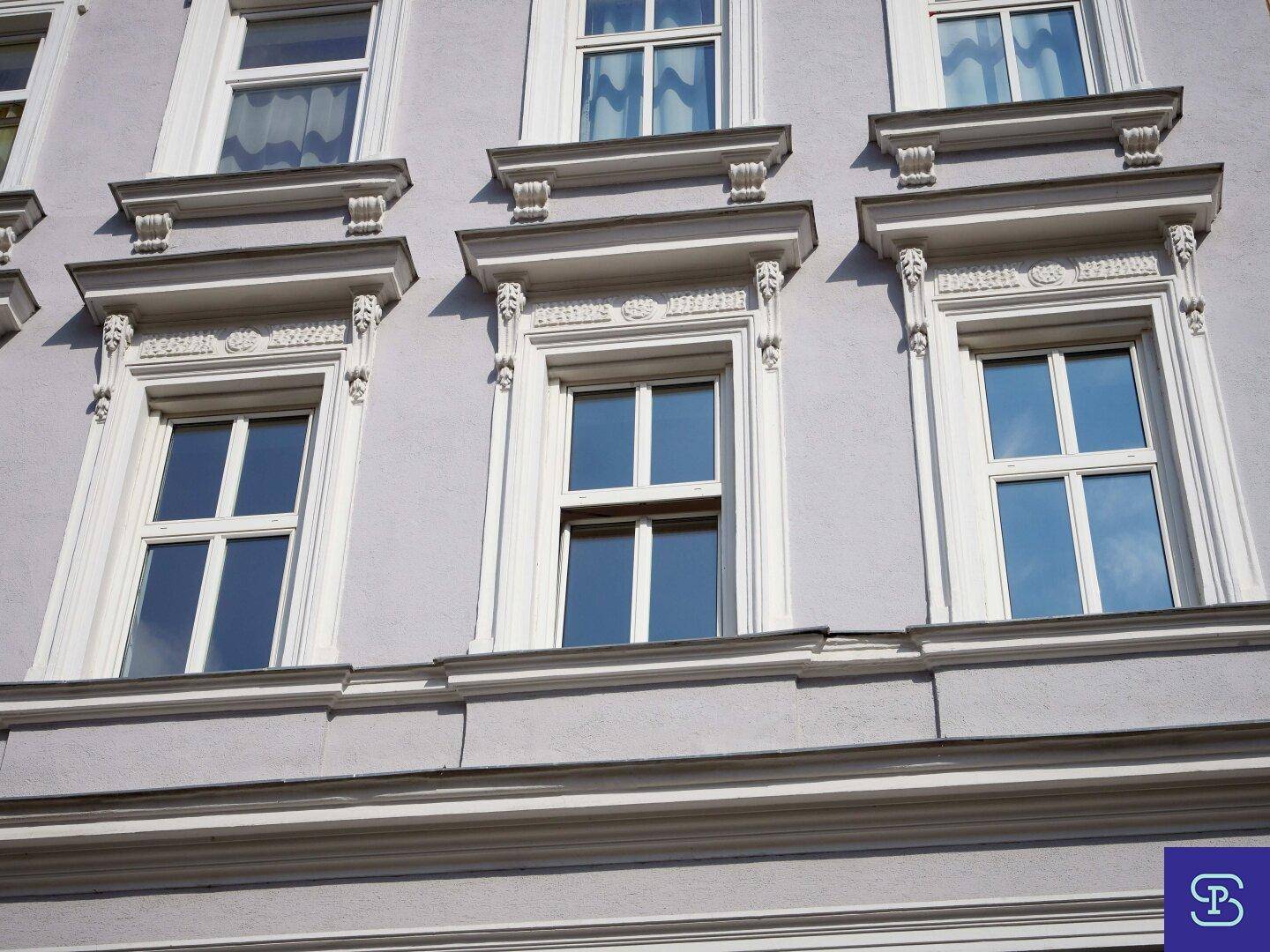 Detailansicht der eleganten Fensterfassade eines Altbaus mit Stuckverzierungen und weißen Rahmen.