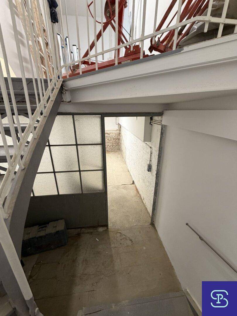 Treppenhaus mit Metallgeländer und Zugang zu einem Kellerraum durch eine Glastür.