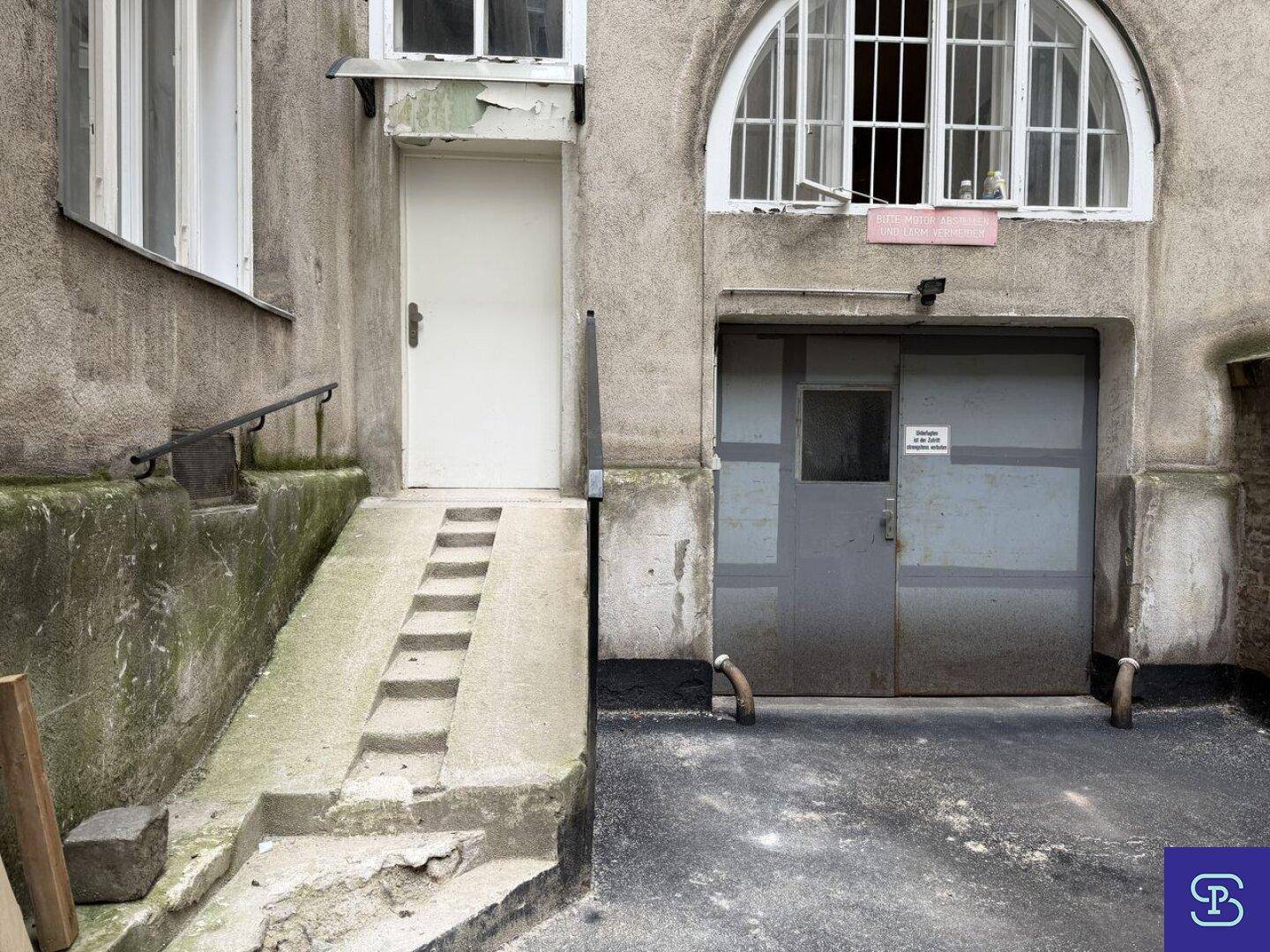 Gebäudefassade mit Eingangstür, Rampe und Garagentor, zeigt den Zugang zum Gebäude.
