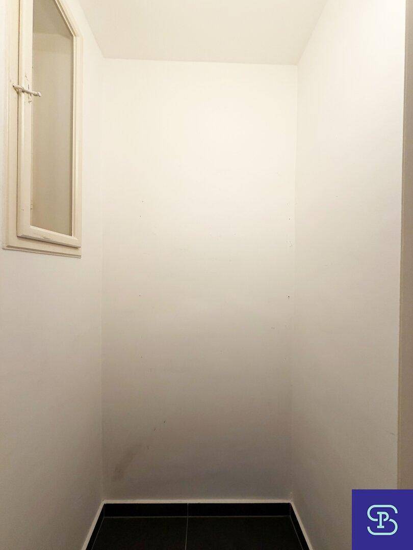 Kleiner, heller Raum mit Fenster und dunklem Fliesenboden, ideal als Abstellraum.