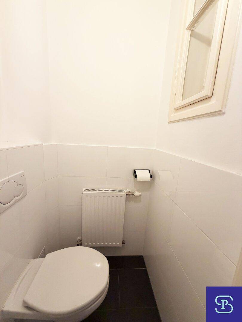 Separate Gästetoilette mit Fenster, Wand-WC und Heizkörper, hell gefliest.