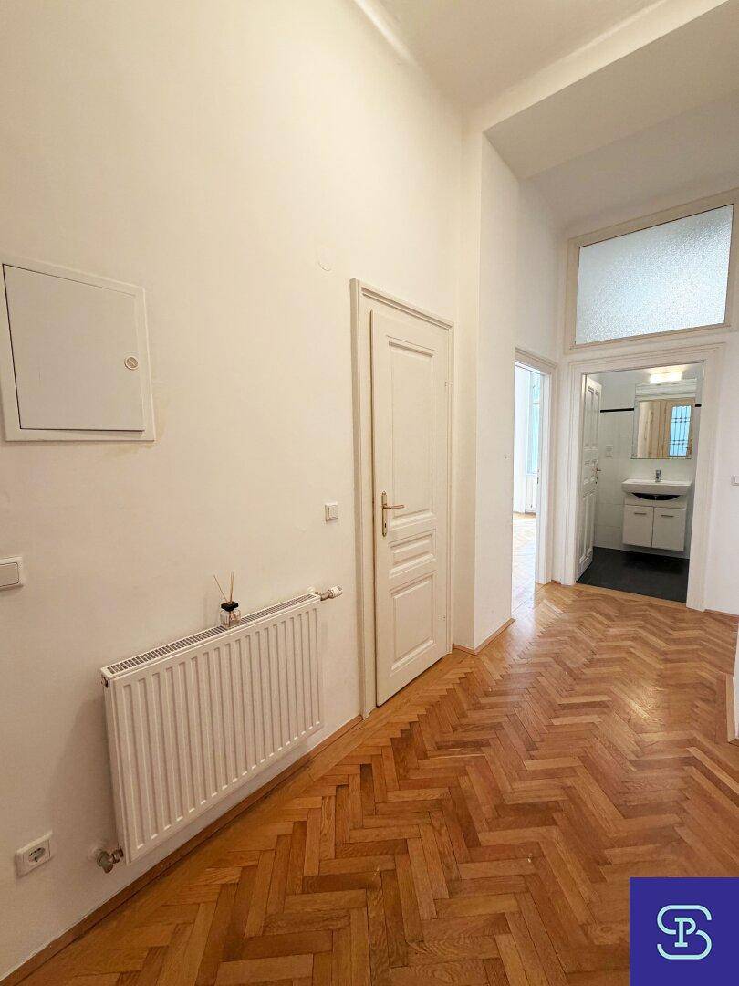 Heller Flur mit Fischgrätparkettboden und Zugang zu einem Badezimmer mit Waschbecken.