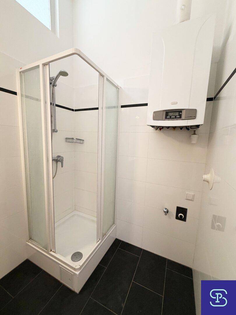Badezimmer mit Duschkabine, Gastherme und weißen Fliesen, funktional eingerichtet.