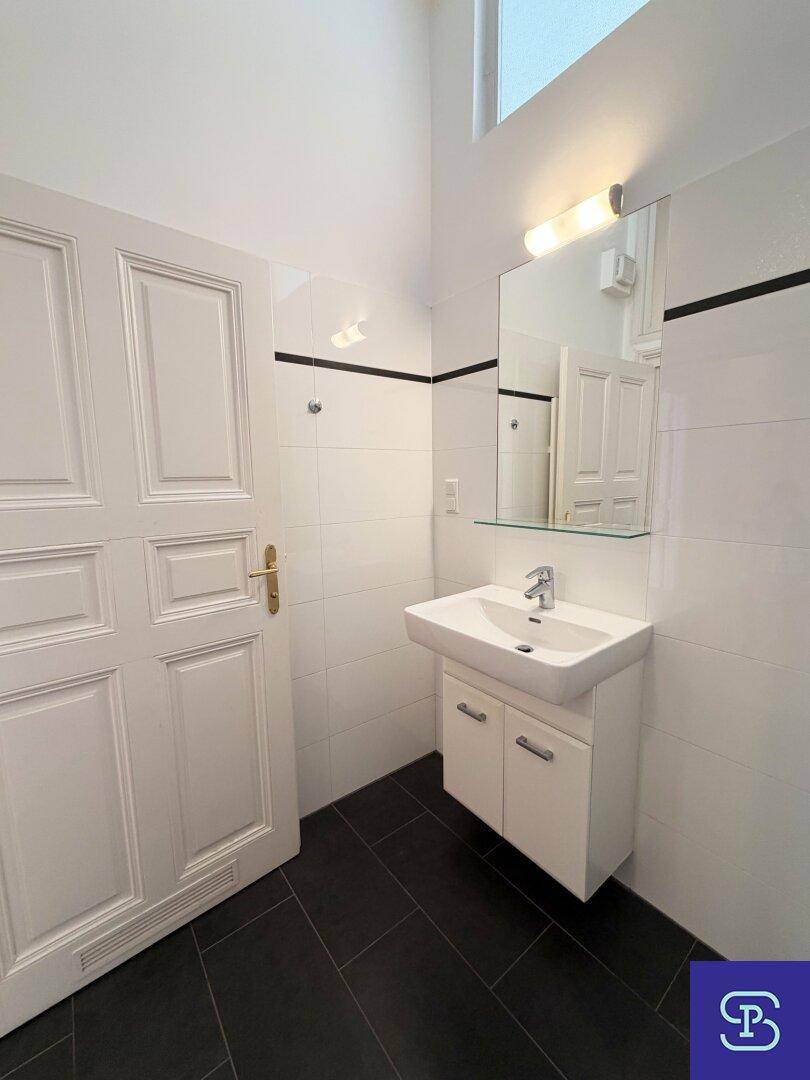 Badezimmer mit modernem Waschbecken, Spiegel und weißen Fliesen, gut beleuchtet.