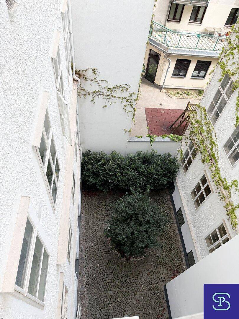 Blick von oben in einen begrünten Innenhof mit Kopfsteinpflaster und bewachsenen Fassaden.