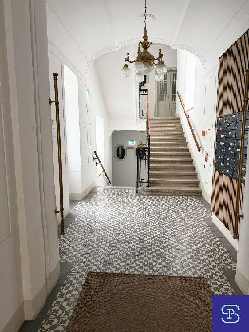 Elegantes Treppenhaus mit gemusterten Fliesen, Holzgeländer und hohen Decken.