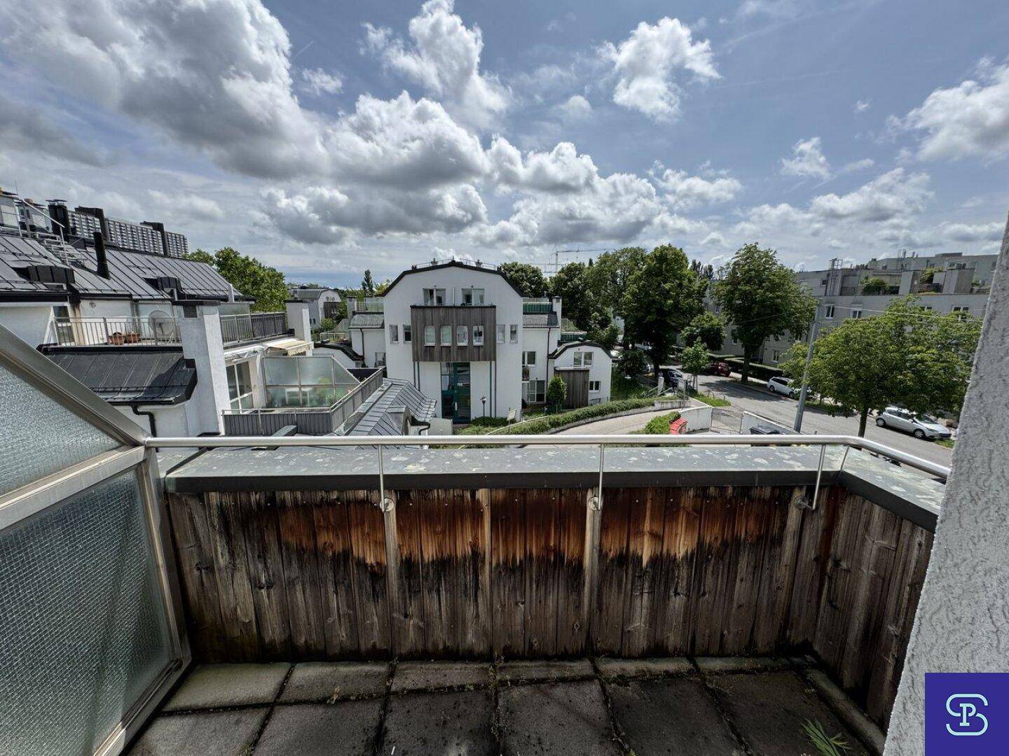 Balkon mit Holzwänden und Blick auf die umliegende Wohnbebauung und Straße.