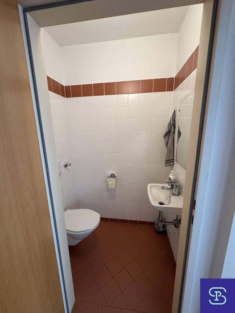 Kleines Gäste-WC mit weißen Wandfliesen, Terrakotta-Boden und einem Waschbecken.