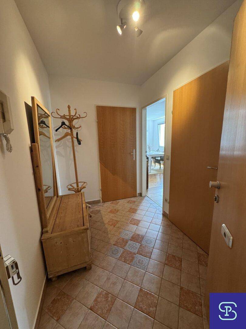 Eingangsbereich mit Terrakotta-Fliesenboden, Garderobe und Spiegel, der zu weiteren Räumen führt.