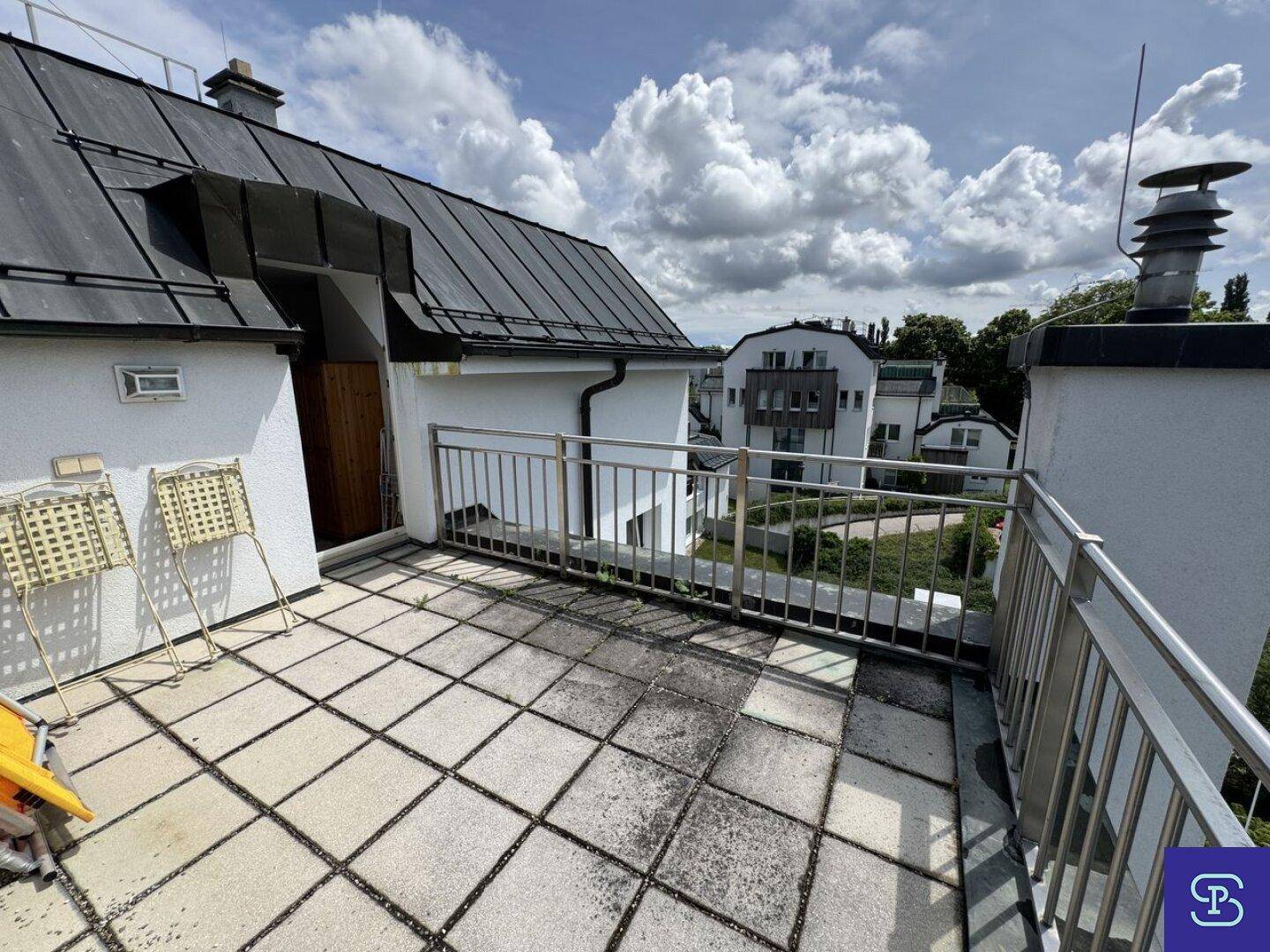 Große Dachterrasse mit Metallgeländer und Blick auf die umliegenden Dächer und Bäume.