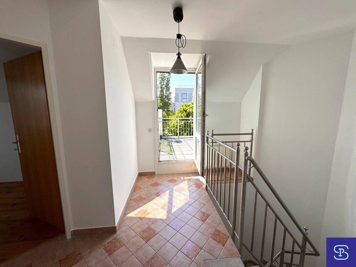 Flur mit Terrakotta-Fliesenboden, Treppe und Zugang zu einem sonnigen Außenbereich.