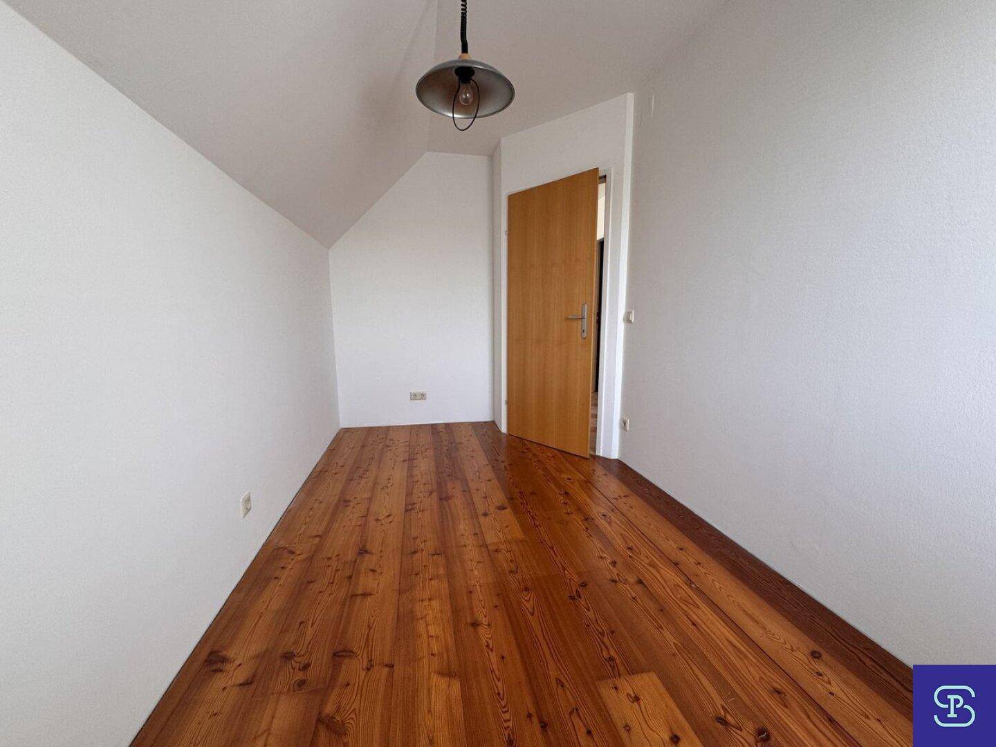 Leeres Zimmer mit Holzboden, Dachschräge und einer Holztür, ideal als Kinderzimmer.