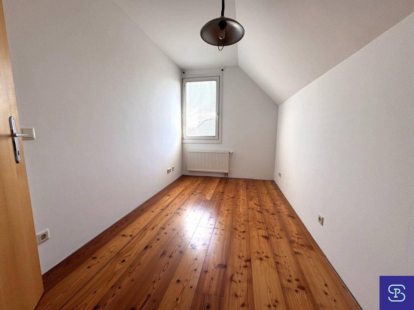 Schlafzimmer mit Dachschräge, Holzdielenboden und einem Fenster für natürliches Licht.