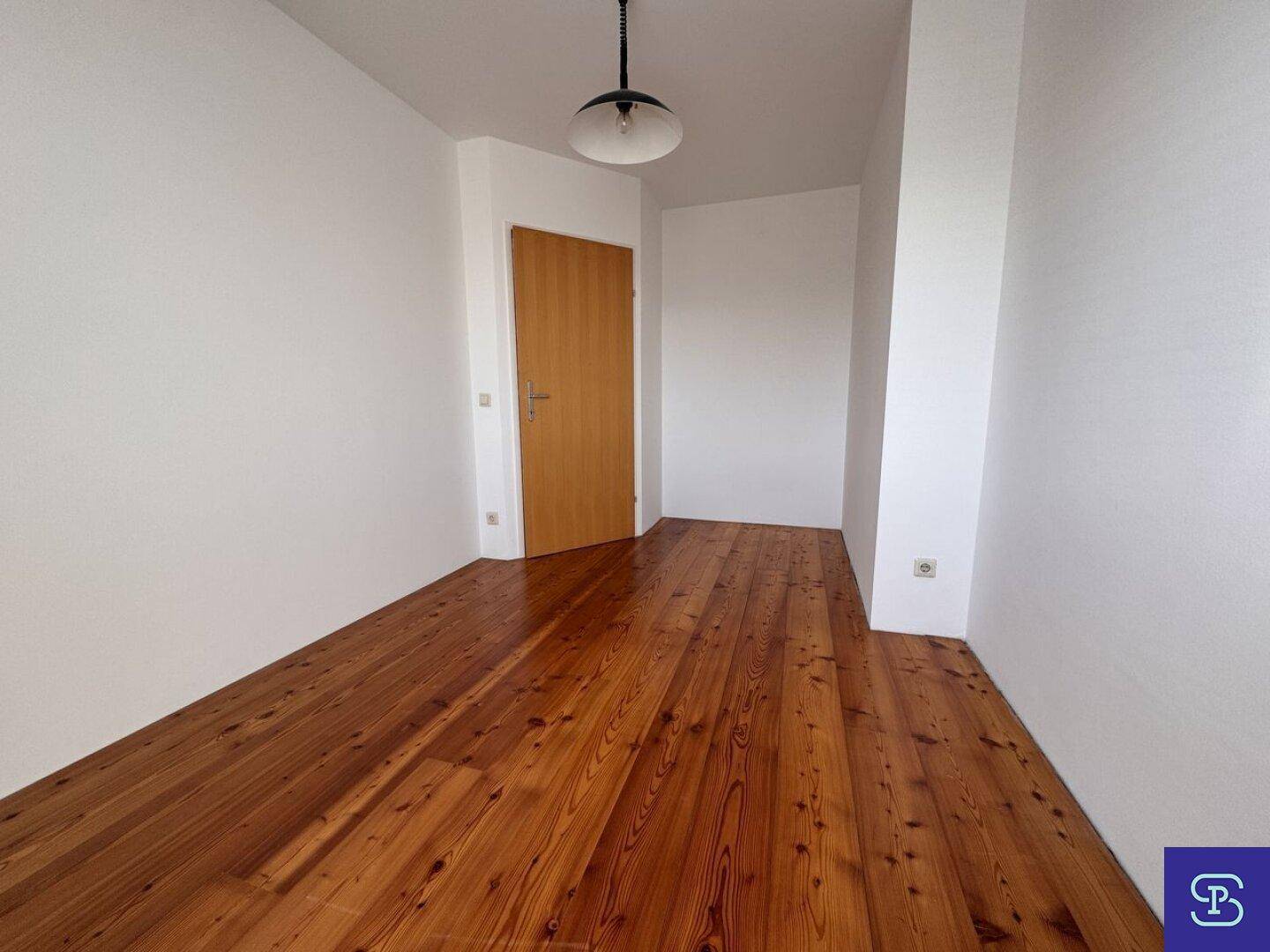 Helles Zimmer mit Holzboden und einer Holztür, bereit zur individuellen Gestaltung.