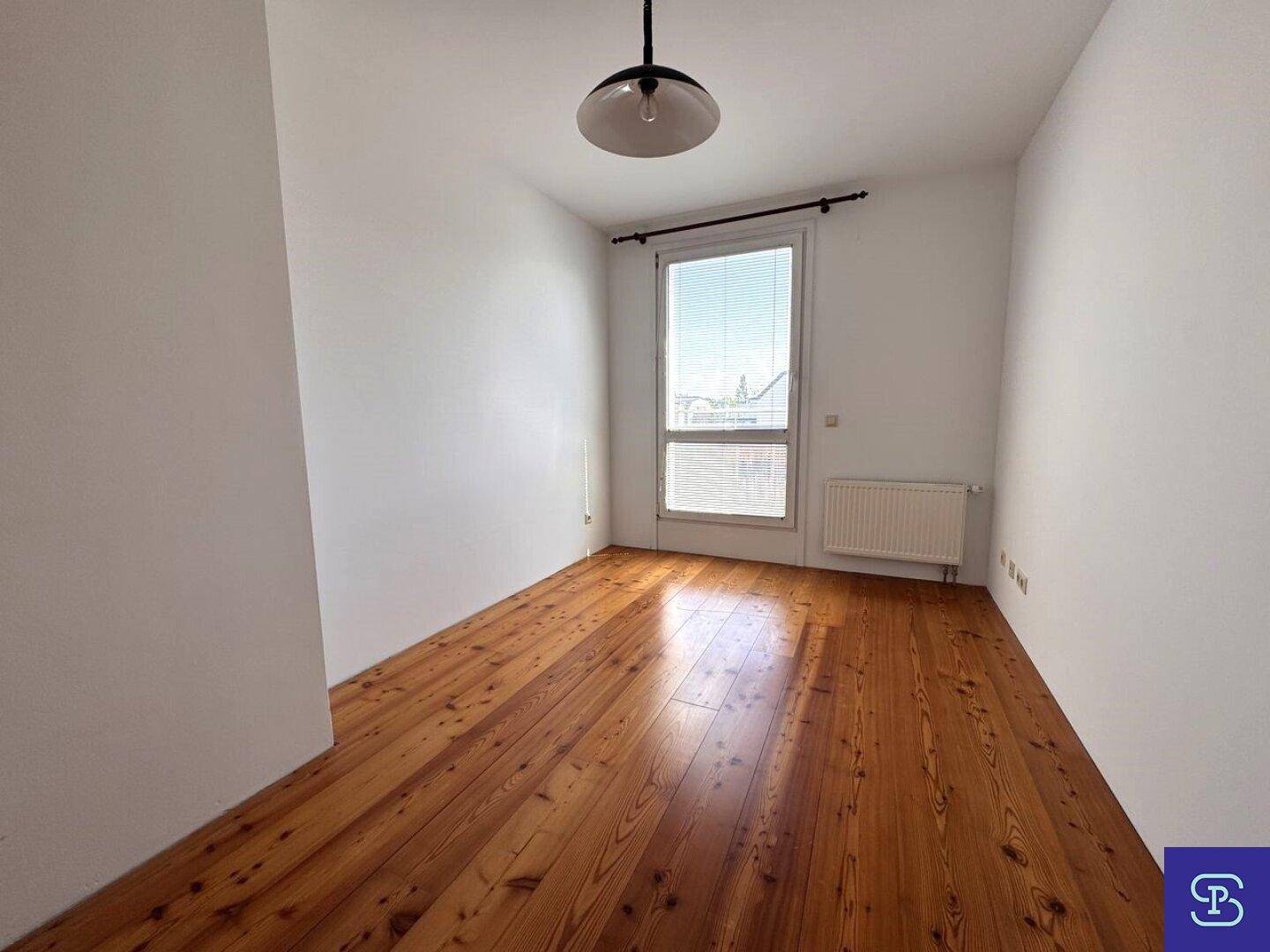 Leeres Schlafzimmer mit Holzdielenboden, weiß gestrichenen Wänden und einem Fenster.