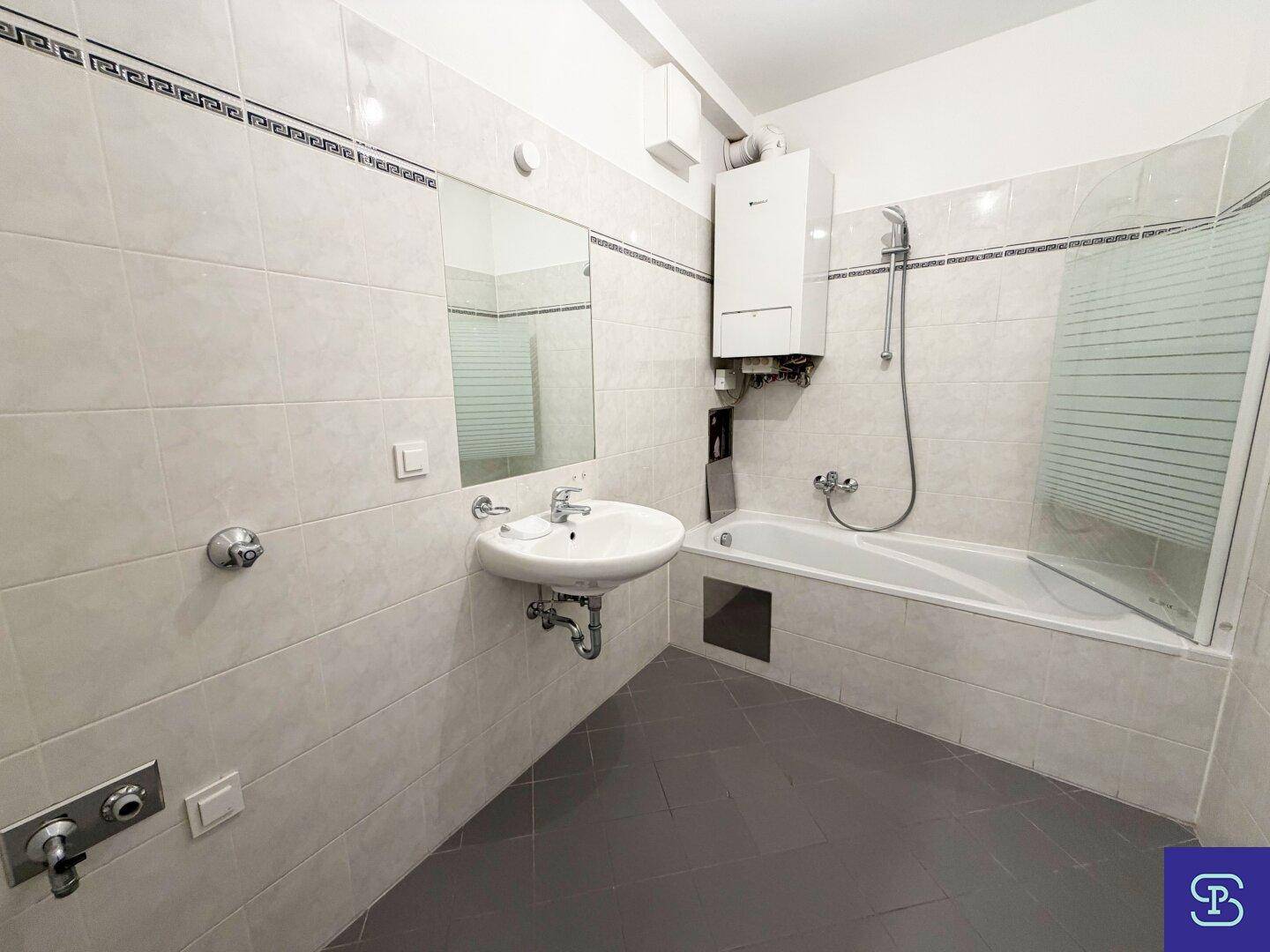 Gefliestes Badezimmer mit Badewanne, Waschbecken und Wandspiegel, inklusive Warmwasserbereiter.