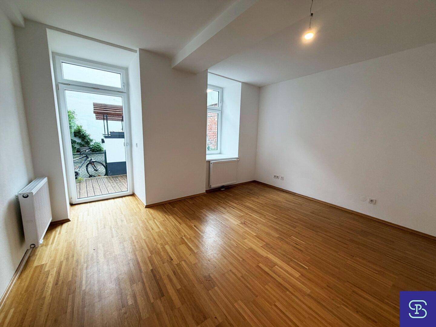 Helles Zimmer mit Parkettboden und direktem Zugang zu einem kleinen Außenbereich durch eine Glastür.