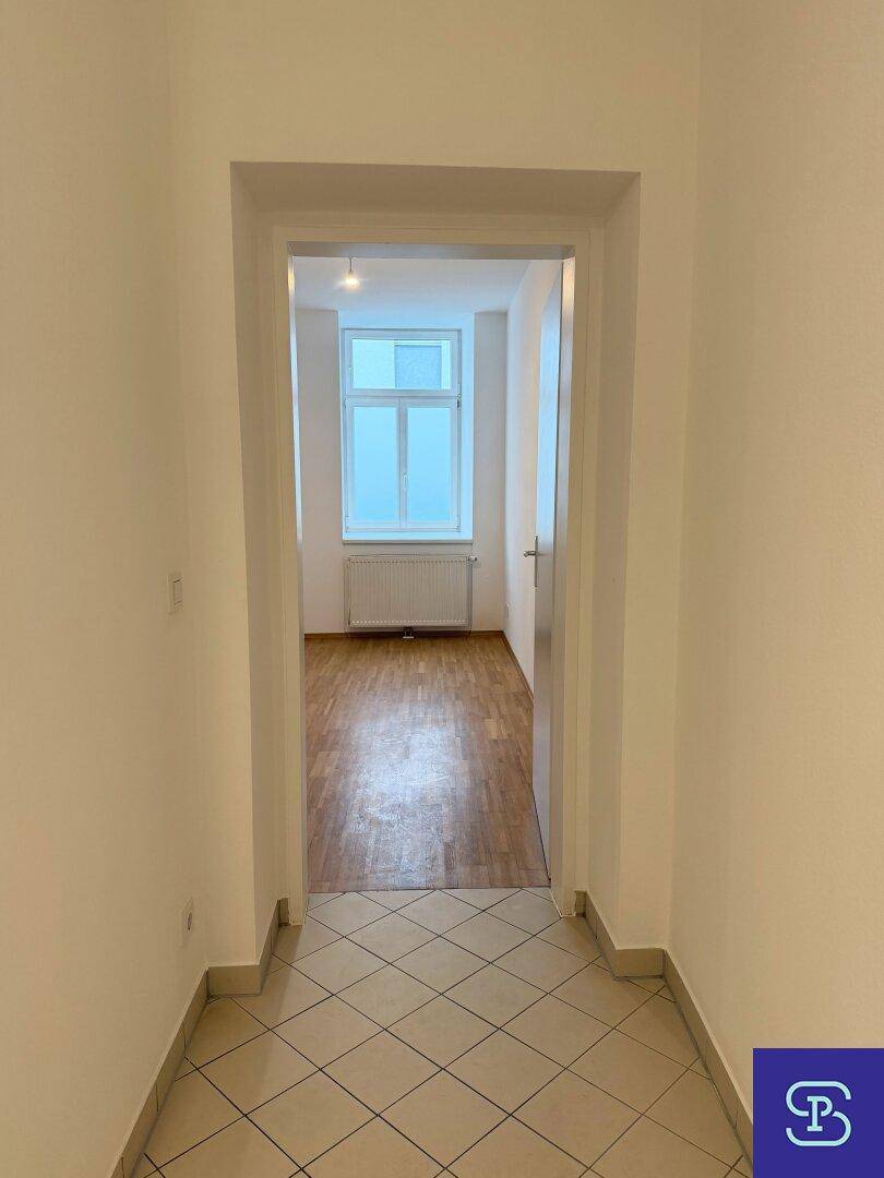 Flur mit Fliesenboden, der zu einem weiteren hellen Zimmer mit Parkettboden führt.