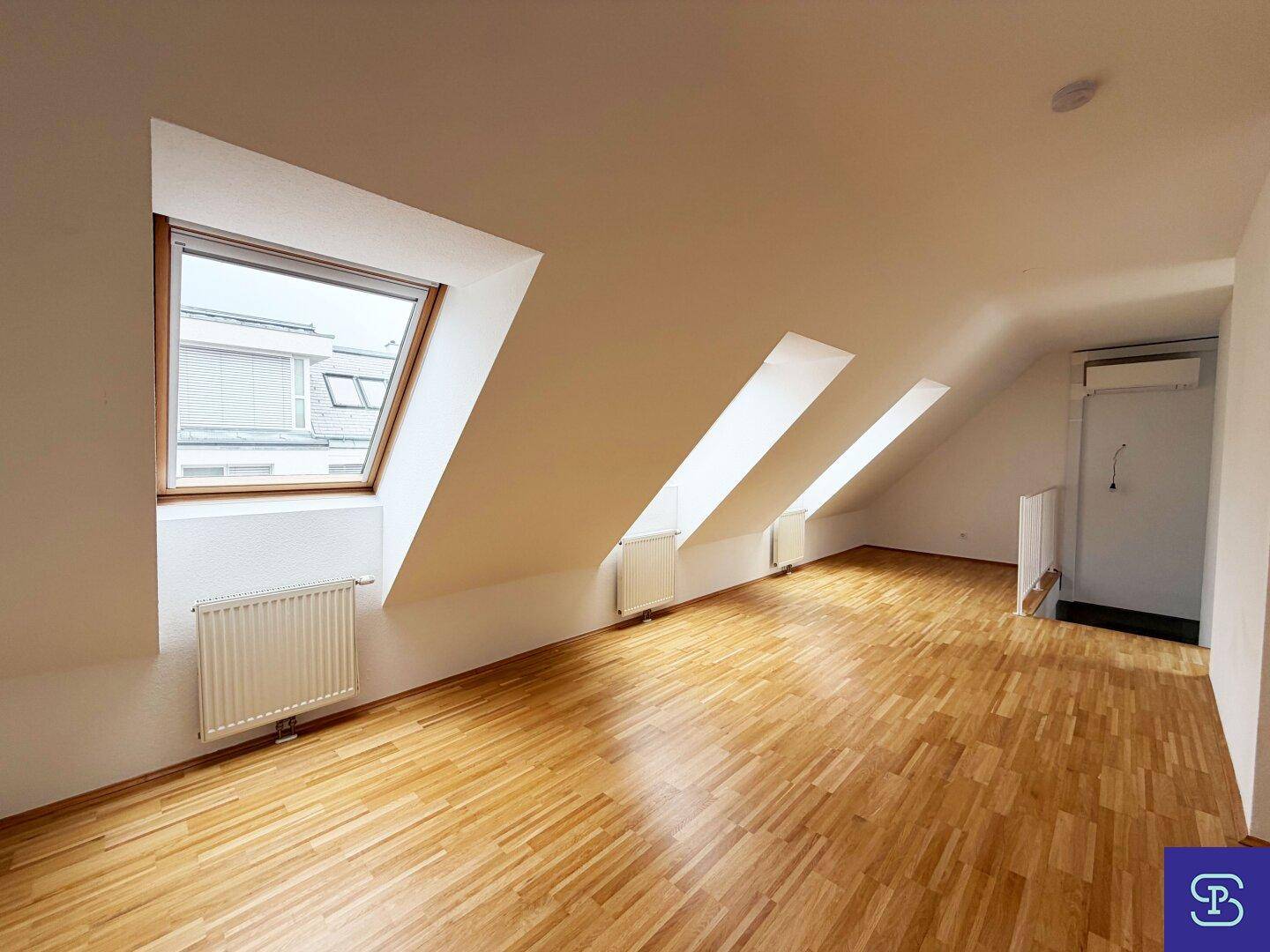 Geräumiger, heller Raum mit Parkettboden und mehreren Dachfenstern, ideal als Wohn- oder Schlafzimmer.