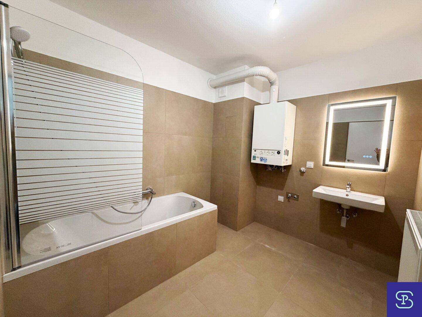 Modernes Badezimmer mit beigefarbenen Fliesen, Badewanne mit Duschabtrennung und beleuchtetem Spiegel.