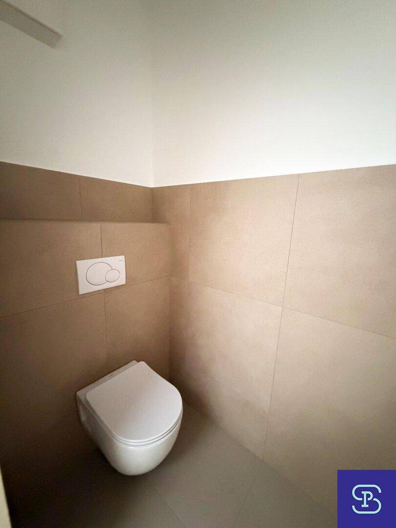 Modernes Gäste-WC mit wandhängender Toilette und beigefarbenen Wandfliesen.