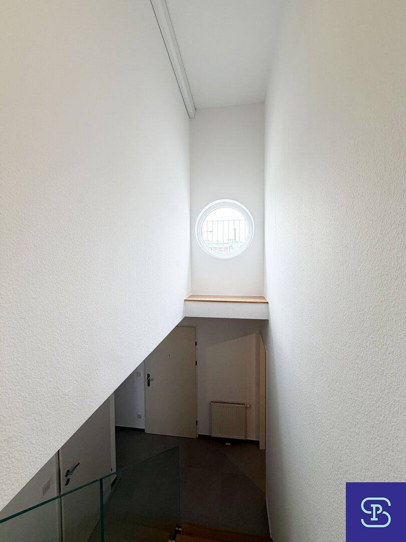 Heller Treppenaufgang mit einem markanten runden Fenster, das natürliches Licht spendet.