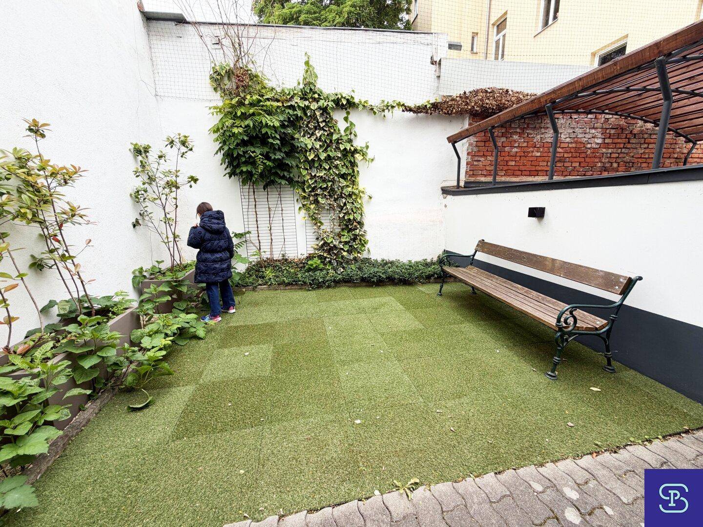 Kleiner, pflegeleichter Gartenbereich mit Kunstrasen und einer Holzbank zum Entspannen.