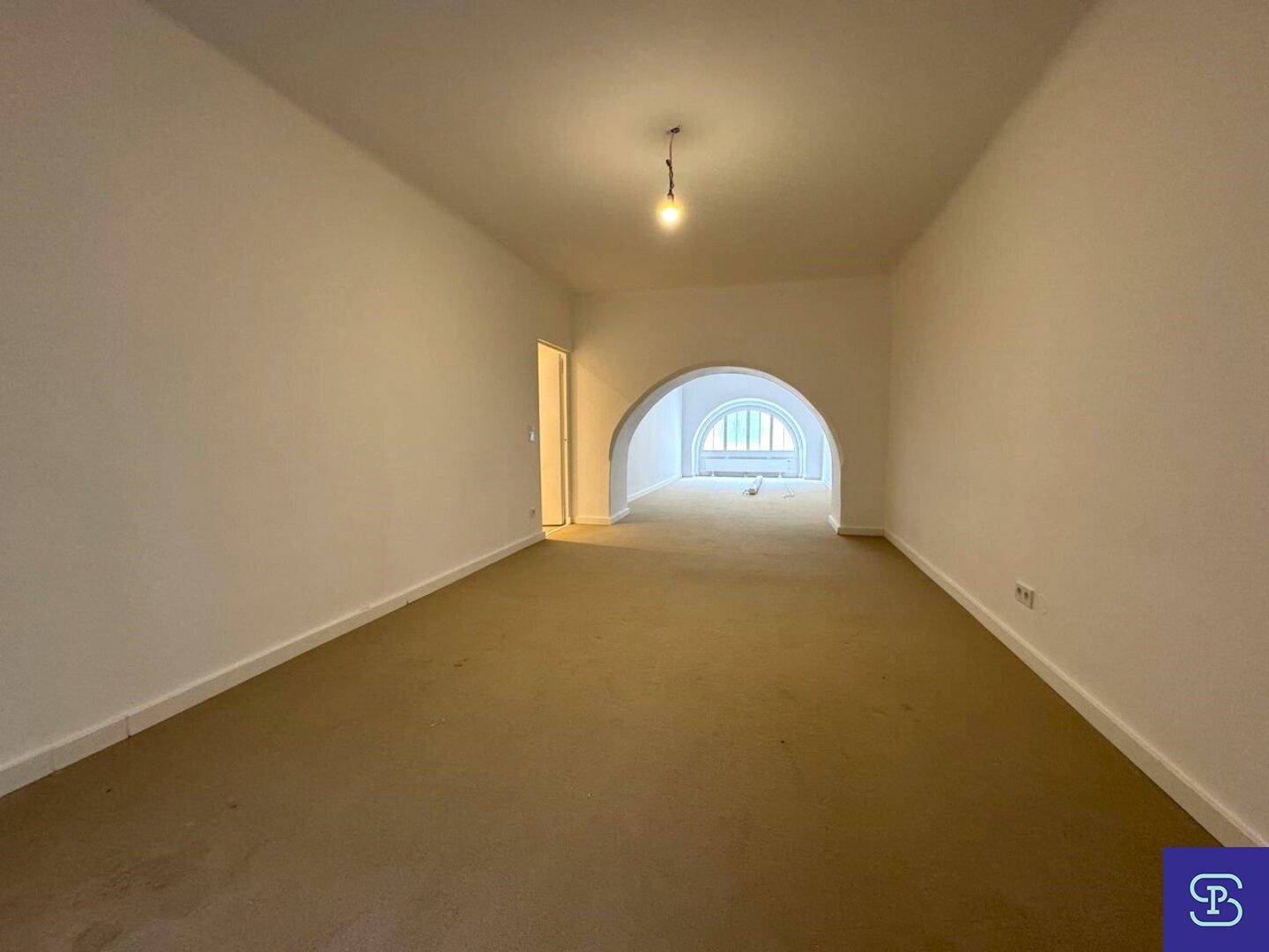 Geräumiges Zimmer mit Teppichboden und einem Rundbogen, der zu einem hellen Bereich führt.