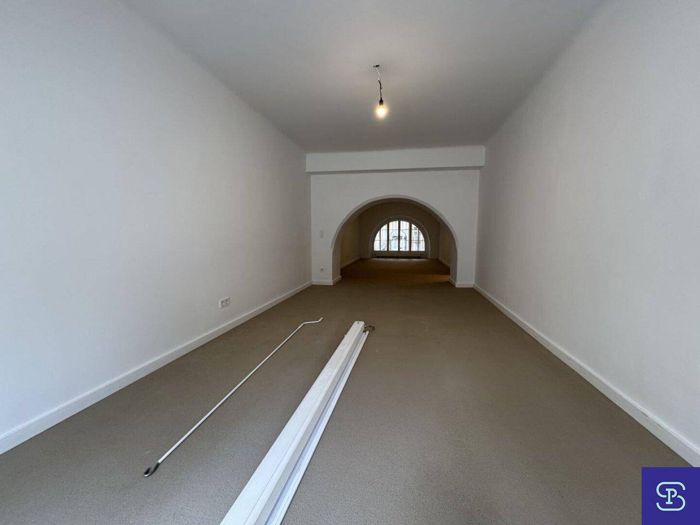 Helles Zimmer mit Teppichboden und einem eleganten Rundbogen, der einen weiteren Bereich verbindet.