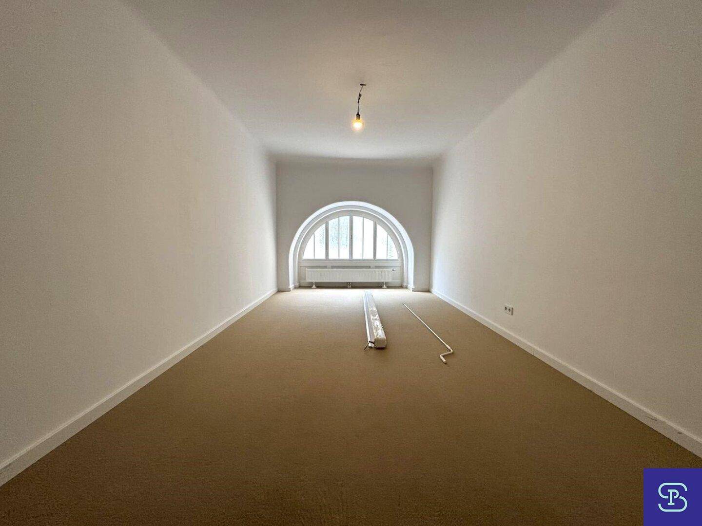 Geräumiges Zimmer mit Teppichboden und einem markanten Rundbogenfenster.
