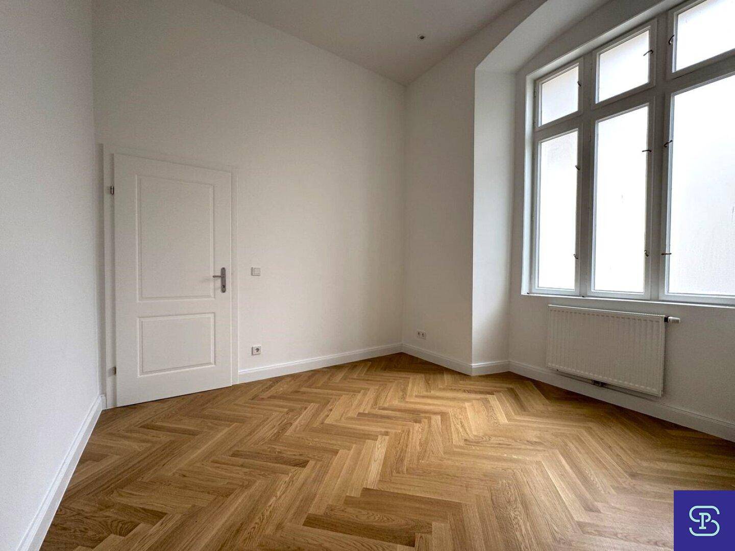 Helles Zimmer mit Fischgrätparkett und einem großen Fenster, ideal für Schlaf- oder Arbeitsbereich.