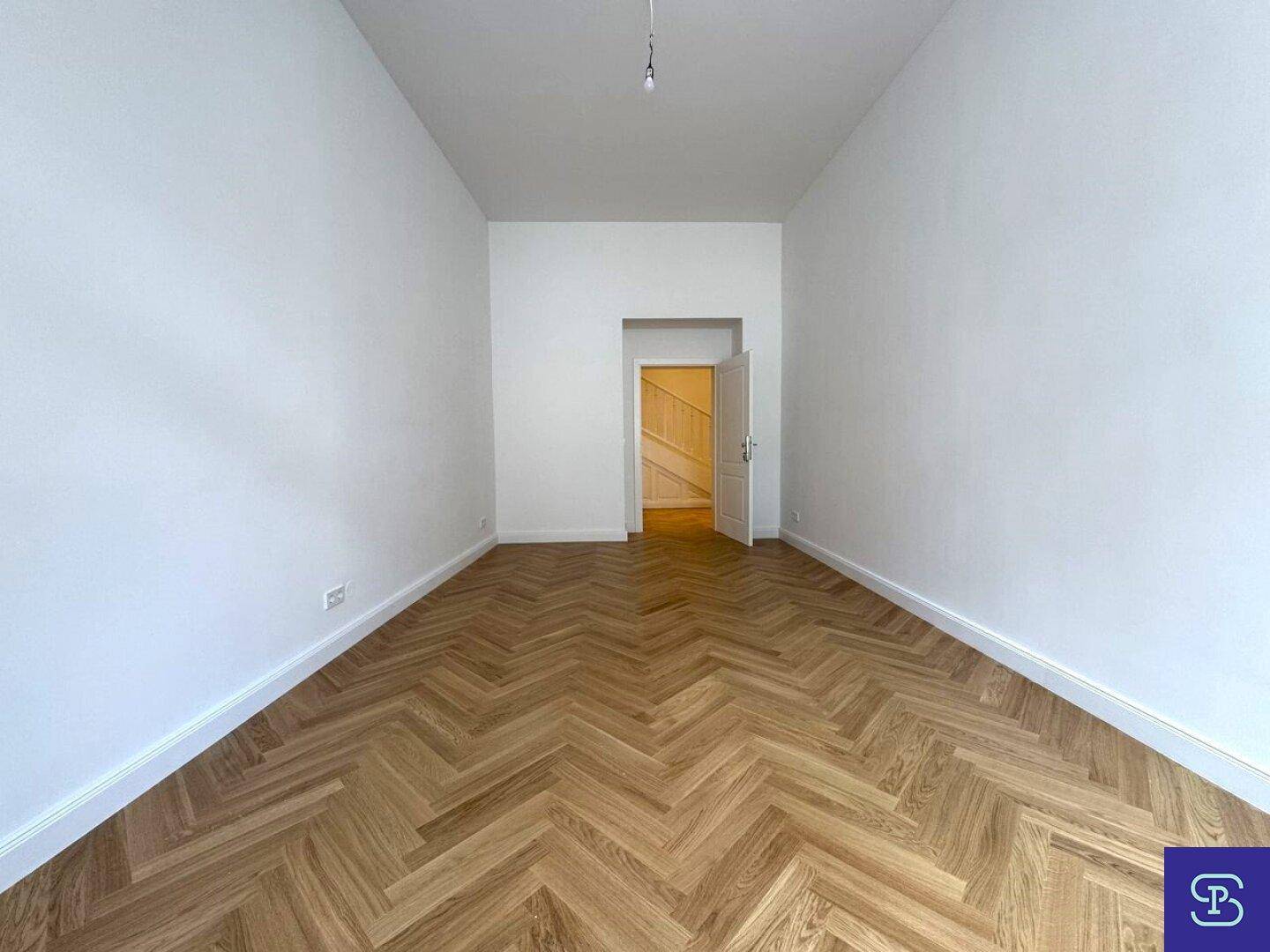 Langes Zimmer mit Fischgrätparkett und offenem Zugang zu einem Flur.