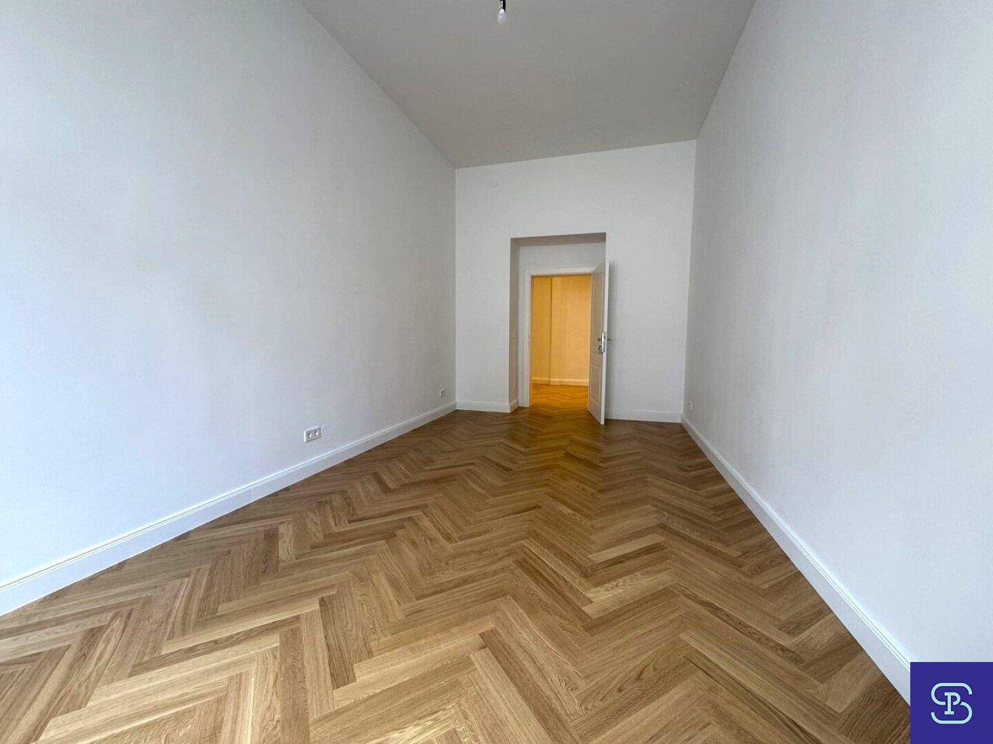 Geräumiges Zimmer mit Fischgrätparkett und Zugang zu einem weiteren Raum.