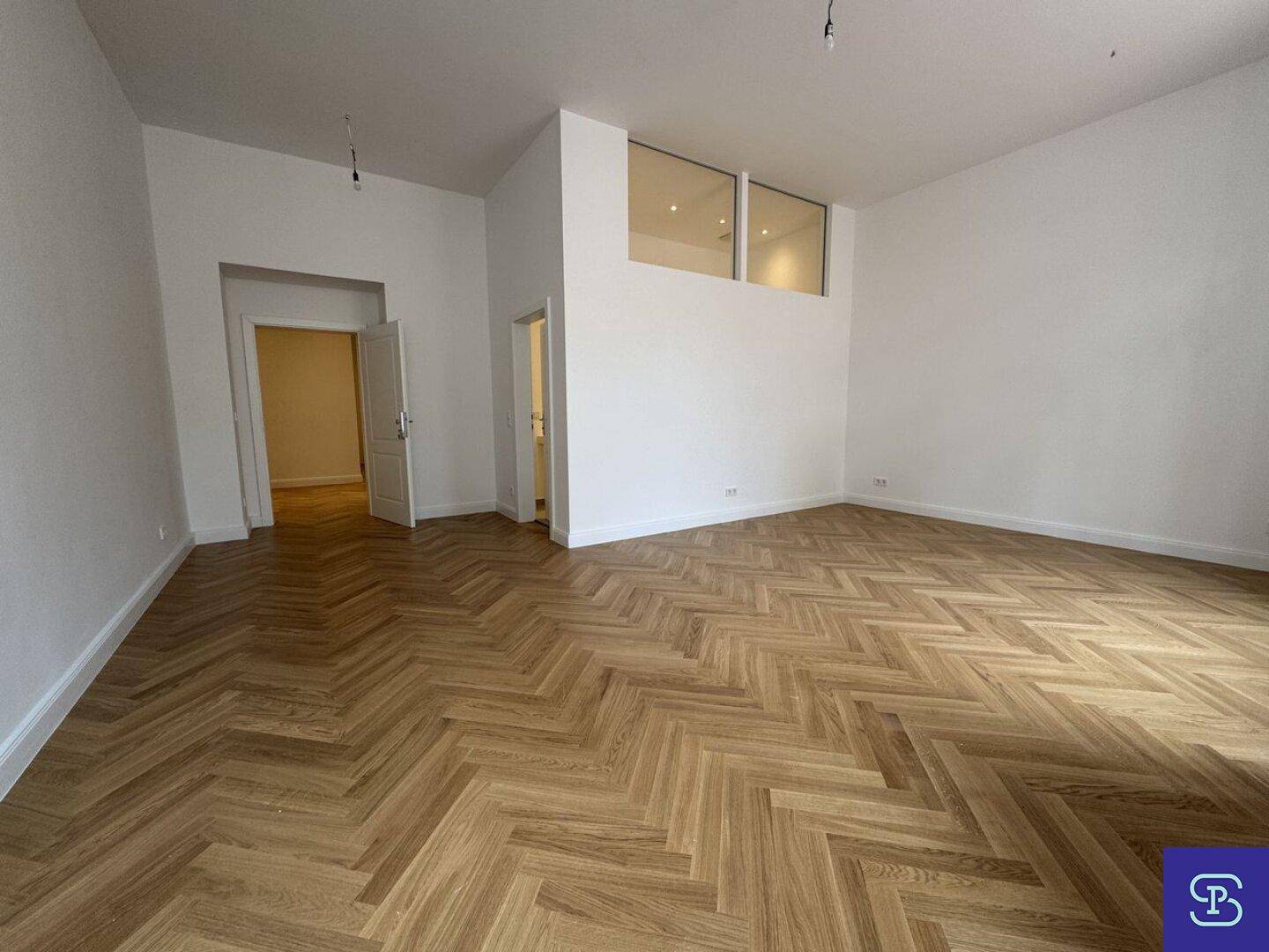 Großzügiges Wohnzimmer mit Fischgrätparkett und Zugang zu weiteren Räumen.