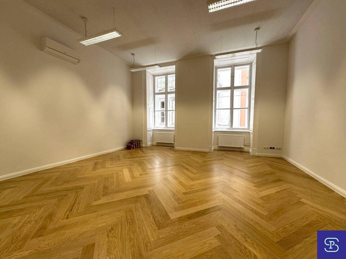 Großer Büroraum mit klassischem Fischgrätparkett, hohen Fenstern und moderner Klimaanlage für angenehmes Raumklima.