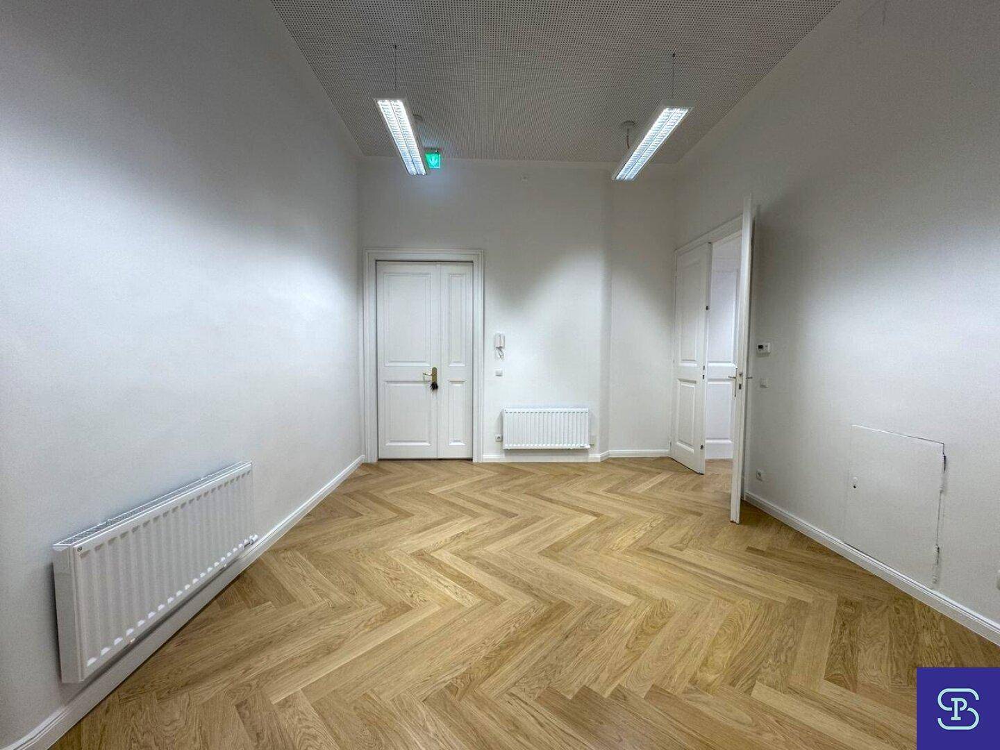 Geräumiger Büroraum mit Fischgrätparkett, hohen Decken und Heizkörpern unter den Fenstern für angenehme Wärme.