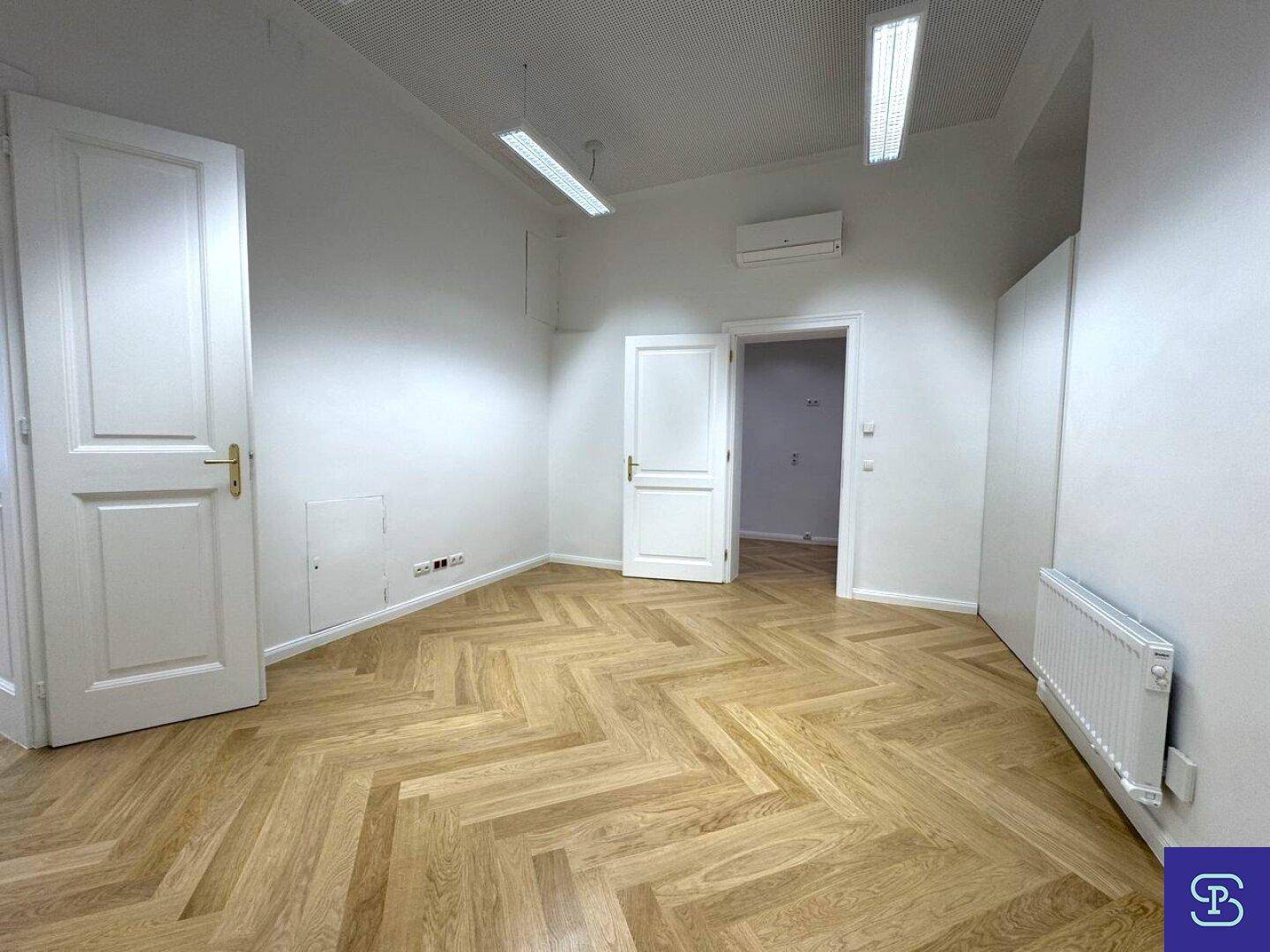 Heller Büroraum mit Fischgrätparkett, hohen Decken und Klimaanlage, ideal für professionelle Nutzung.