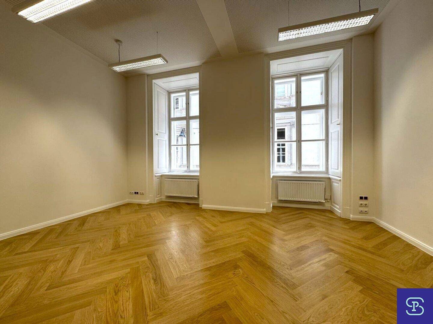 Großer Büroraum mit Fischgrätparkett, hohen Fenstern und Fensterläden, die für Privatsphäre sorgen.