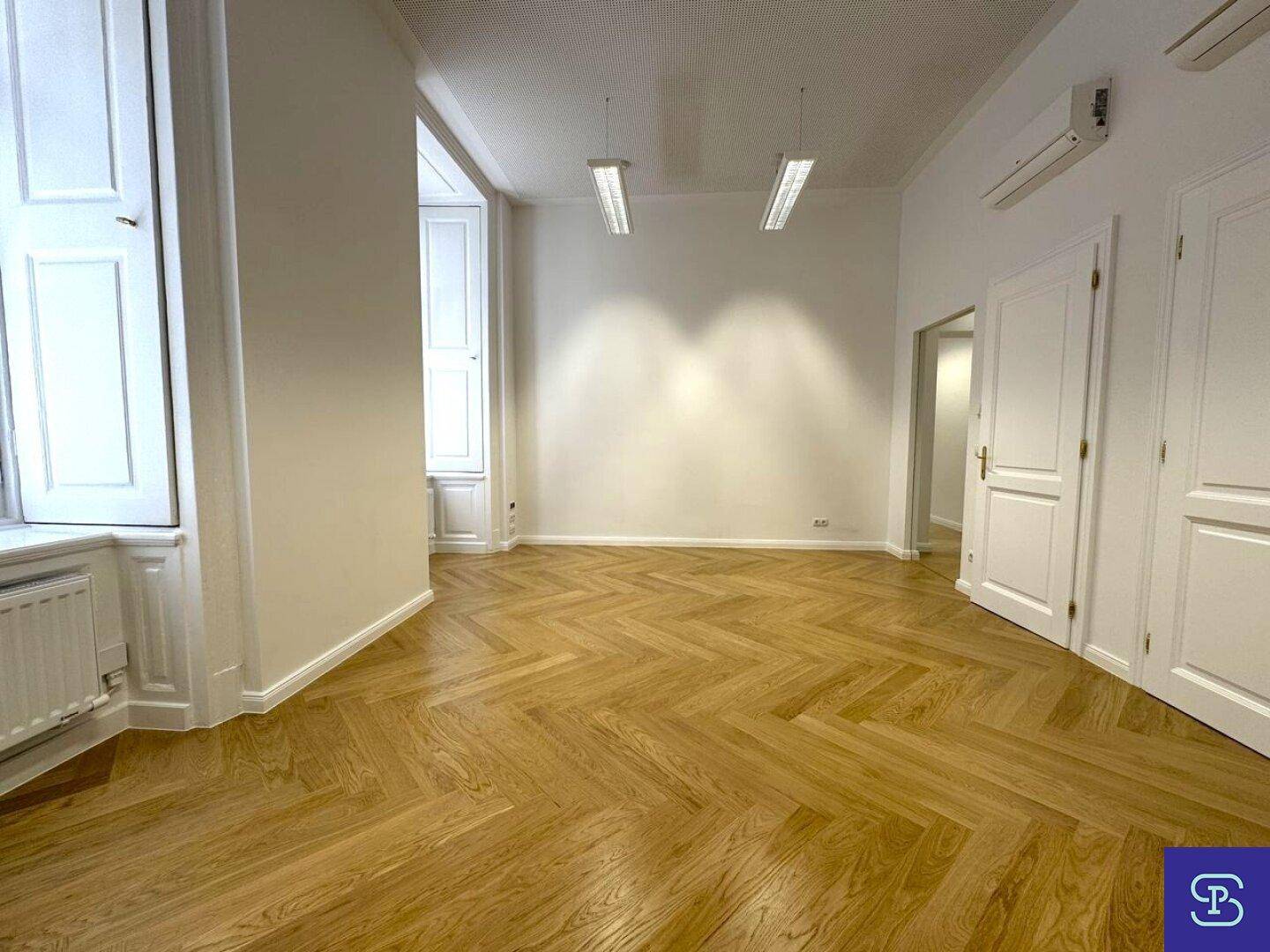 Geräumiger Büroraum mit Fischgrätparkett, hohen Fenstern und Klimaanlage, ideal für ein modernes Arbeitsumfeld.